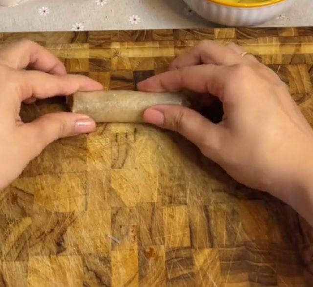 Dùng tay gấp hai bên mép bánh tráng vào, sau đó cuộn tròn từ từ lên trên cho đến hết bánh - Ảnh sưu tầm