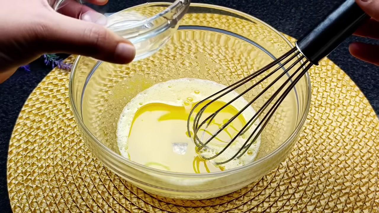 Hỗn hợp trứng và chất lỏng (có thể là sữa) được khuấy đều tay, tạo thành một dung dịch màu trắng đục và nổi bọt.