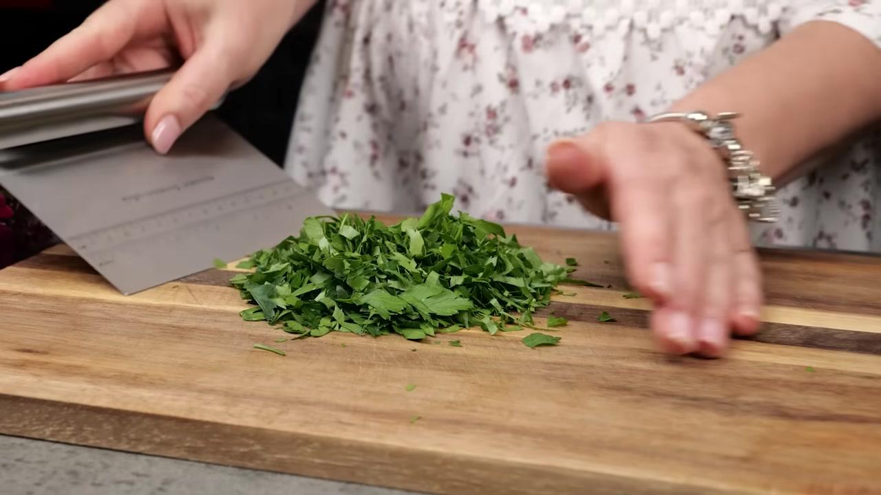 Hai bàn tay đang trộn đều hỗn hợp nhân thịt với rau củ và gia vị trên một miếng thịt lớn đã được cán mỏng.