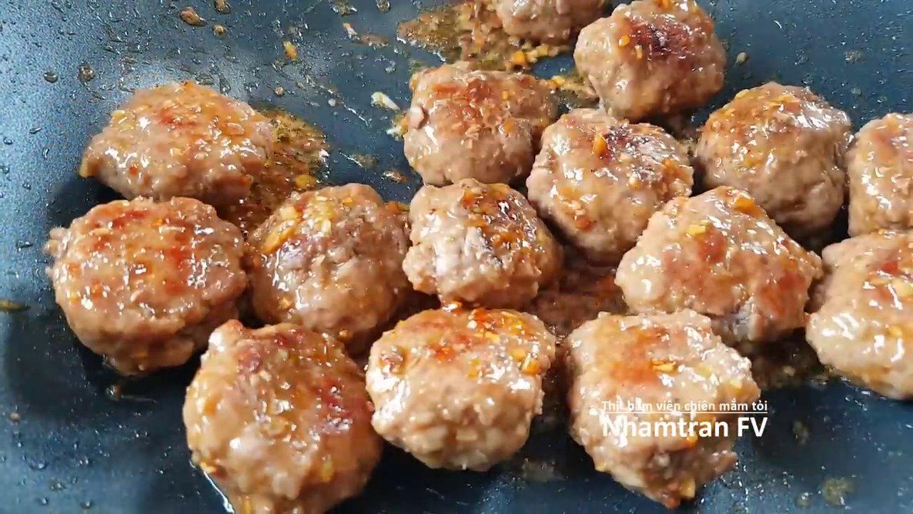 Thịt viên được sốt đều với nước mắm tỏi vàng ươm, rắc thêm hành lá tươi xanh, sẵn sàng để thưởng thức.