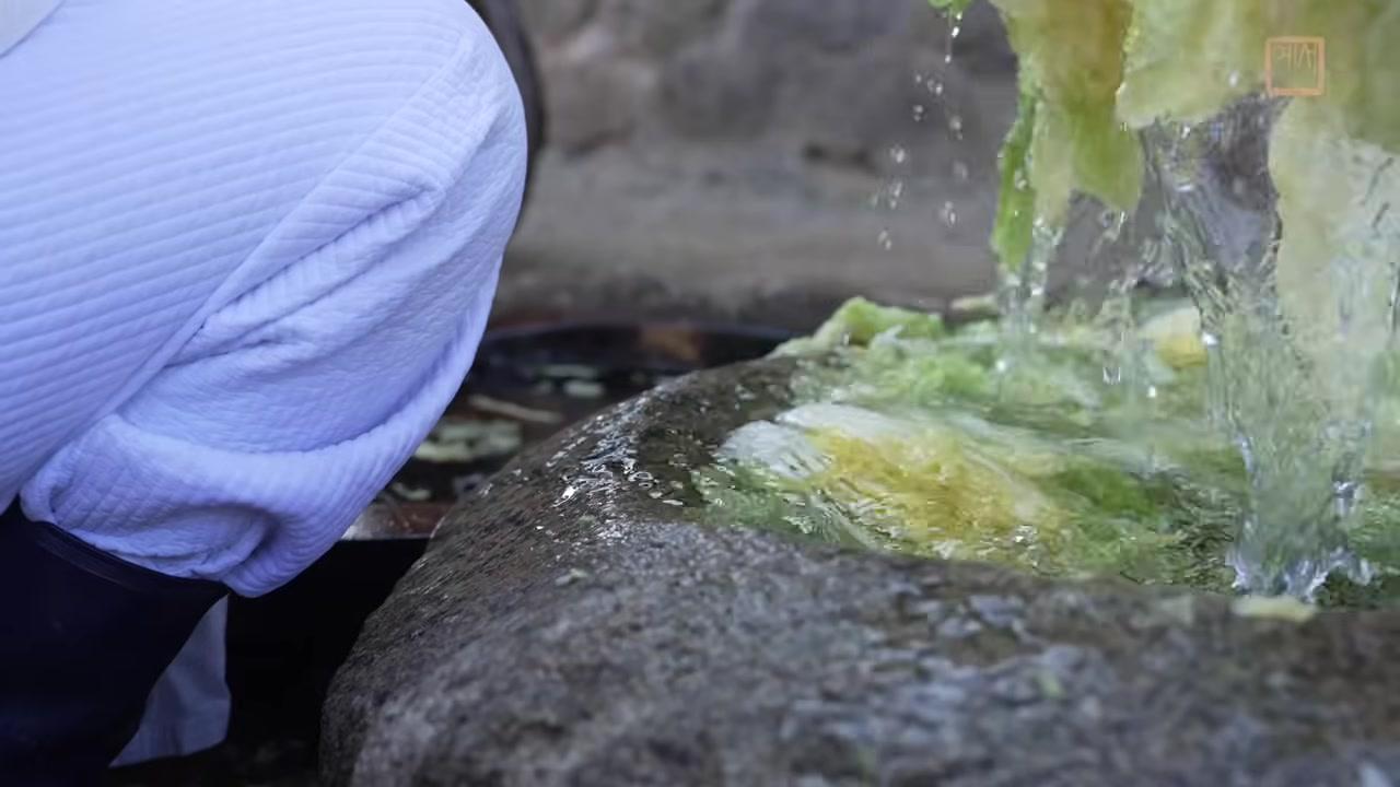 Đôi tay đeo găng đang trộn đều cải thảo với hỗn hợp gia vị đỏ rực trong một chiếc bát đất sét lớn, đảm bảo gia vị thấm đều vào từng thớ rau.